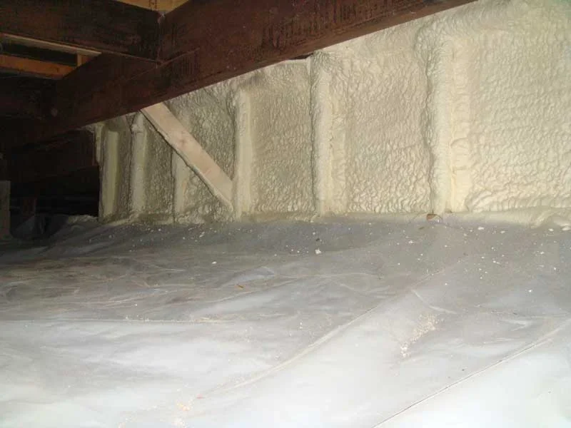 Crawl space with white spray foam insulation applied to rim joist and foundation walls