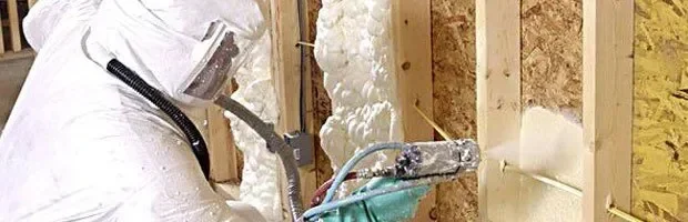 Worker installing fiberglass batt insulation between wooden wall studs with vapor barrier