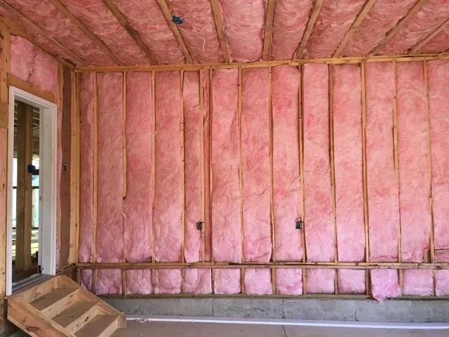 Pink fiberglass insulation batts installed between wood studs in wall and ceiling cavities