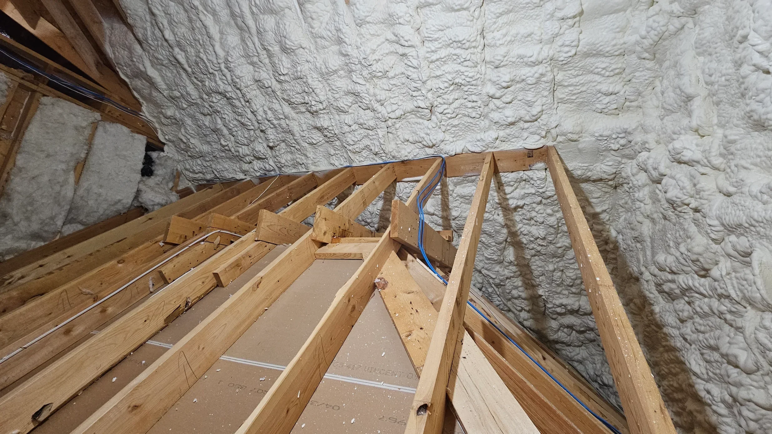 Attic insulation installation showing spray foam on stone walls with wooden rafter framing and electrical wiring
