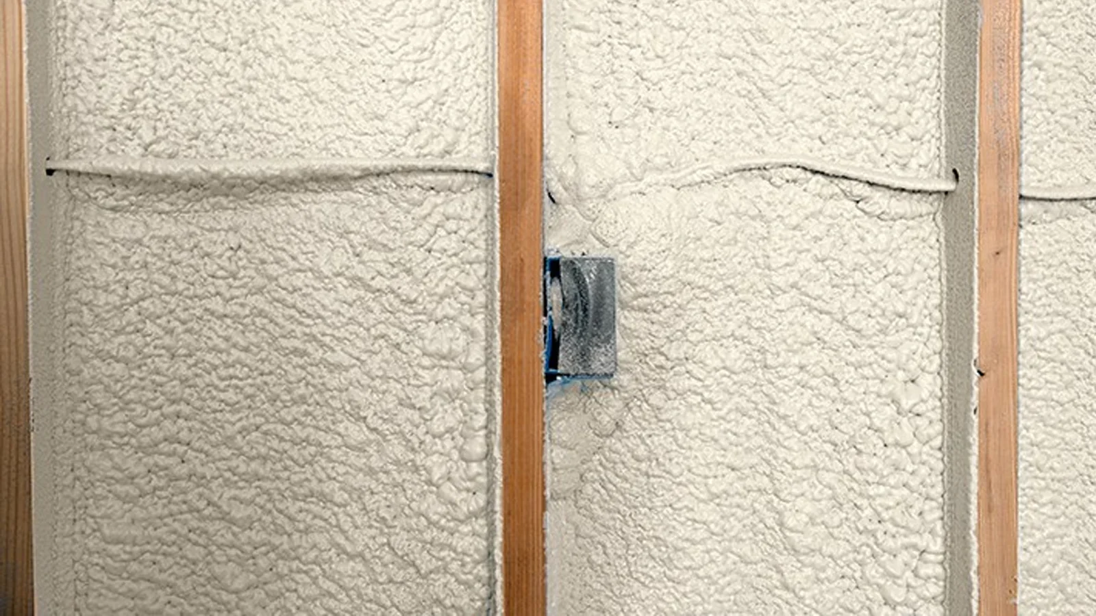 Blown-in wall insulation installed between wooden studs with electrical wiring visible